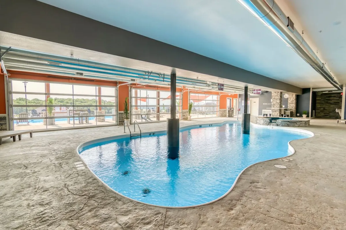 A bright and cheerful indoor swimming pool area, lined with large windows and decorative pillars. The natural light creates a welcoming space for swimming and socializing, regardless of weather outside.