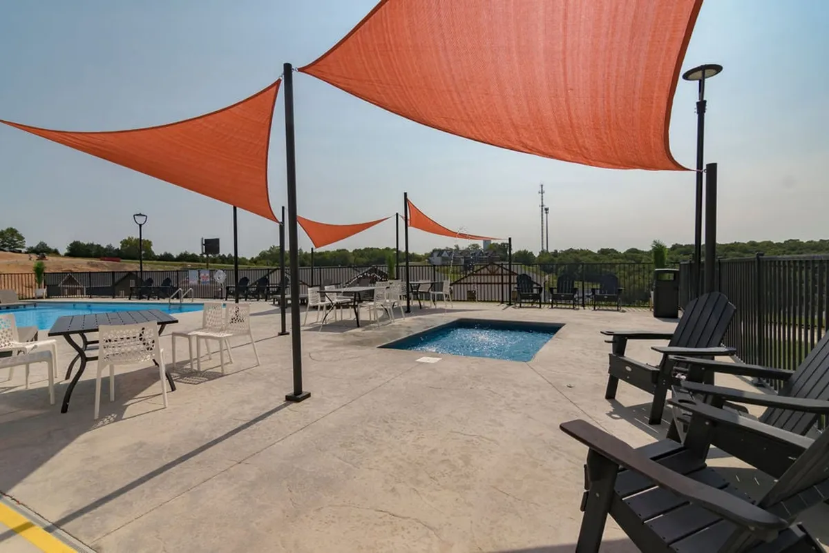 An inviting outdoor pool area complete with modern sail shades and ample seating. The pool is surrounded by a neat patio, perfect for lounging or socializing under both sun and shade.
