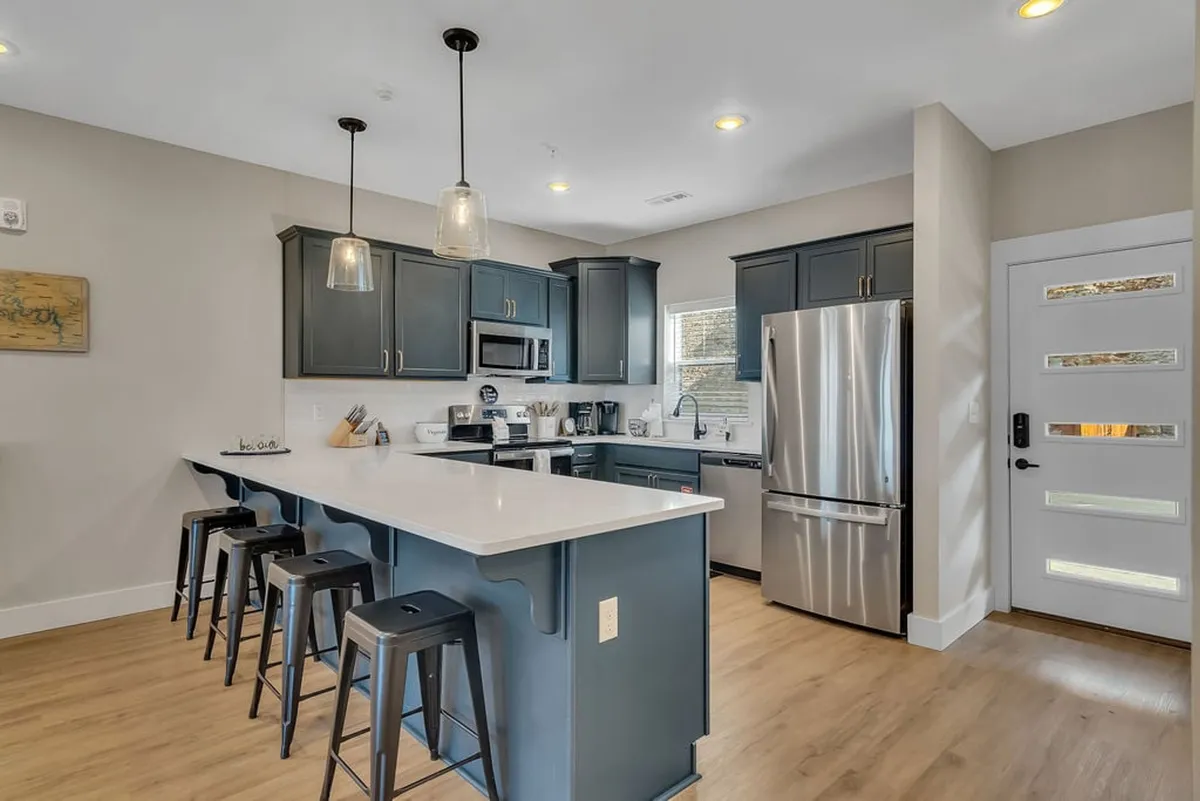 This image features a modern farmhouse kitchen with an island offering seating, stainless steel appliances, dark cabinetry, and a large window that floods the space with natural light. The setting is open and inviting, designed for cooking, socializing, and casual dining, making it well-suited for family gatherings and entertaining guests.
