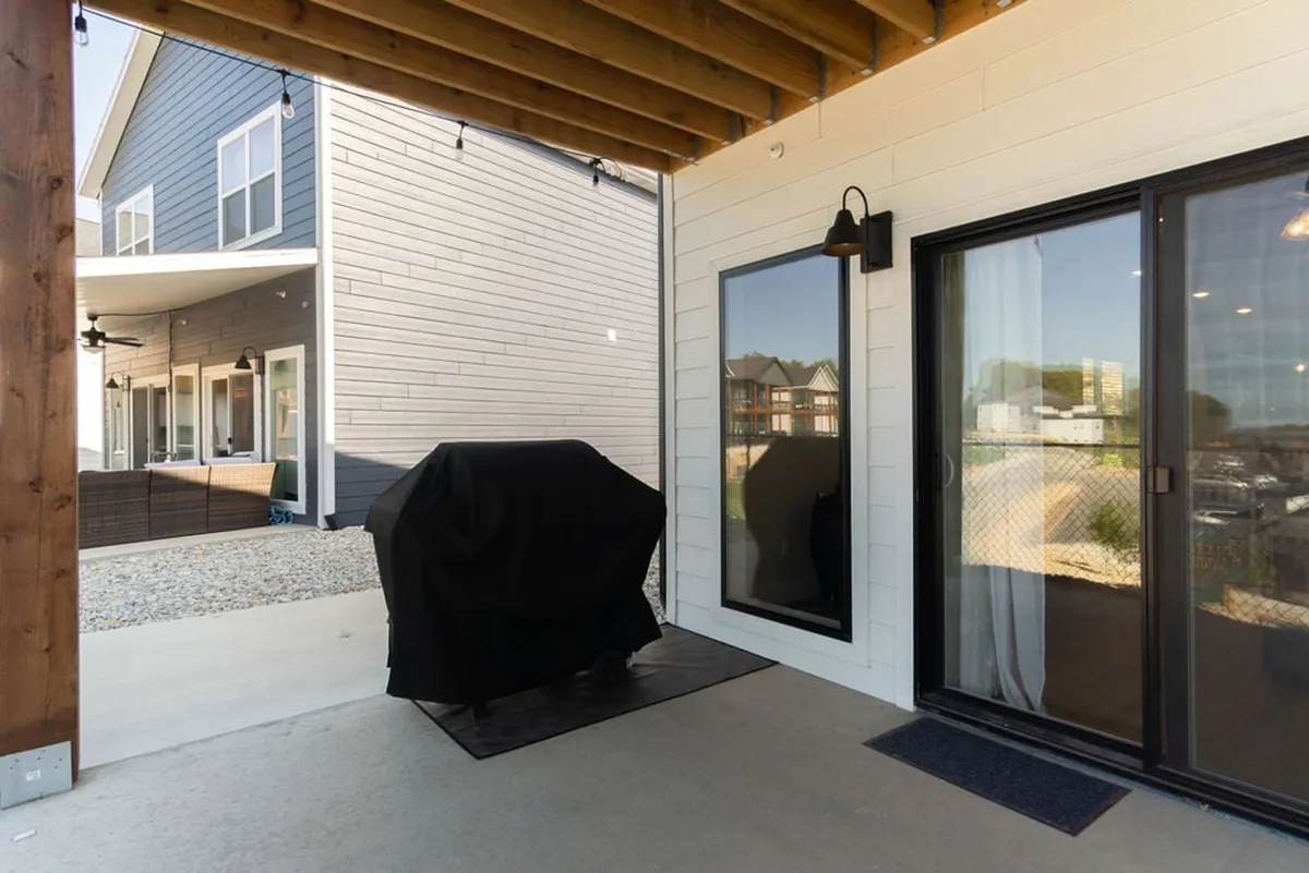An exterior view featuring a covered grill, large windows, and sturdy wooden beams. The area is set up for outdoor dining or relaxing, evoking images of sunsets, celebrations, or peaceful mornings.