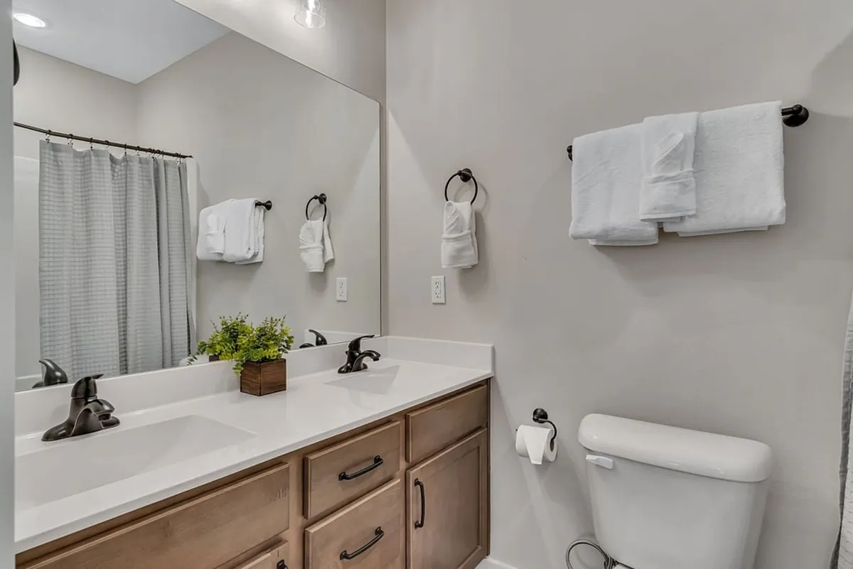 A bright, modern ensuite bathroom with a double vanity, large mirror, towels neatly arranged, and a decorative plant. The space feels fresh, clean, and spa-like, ideal for relaxation and self-care.