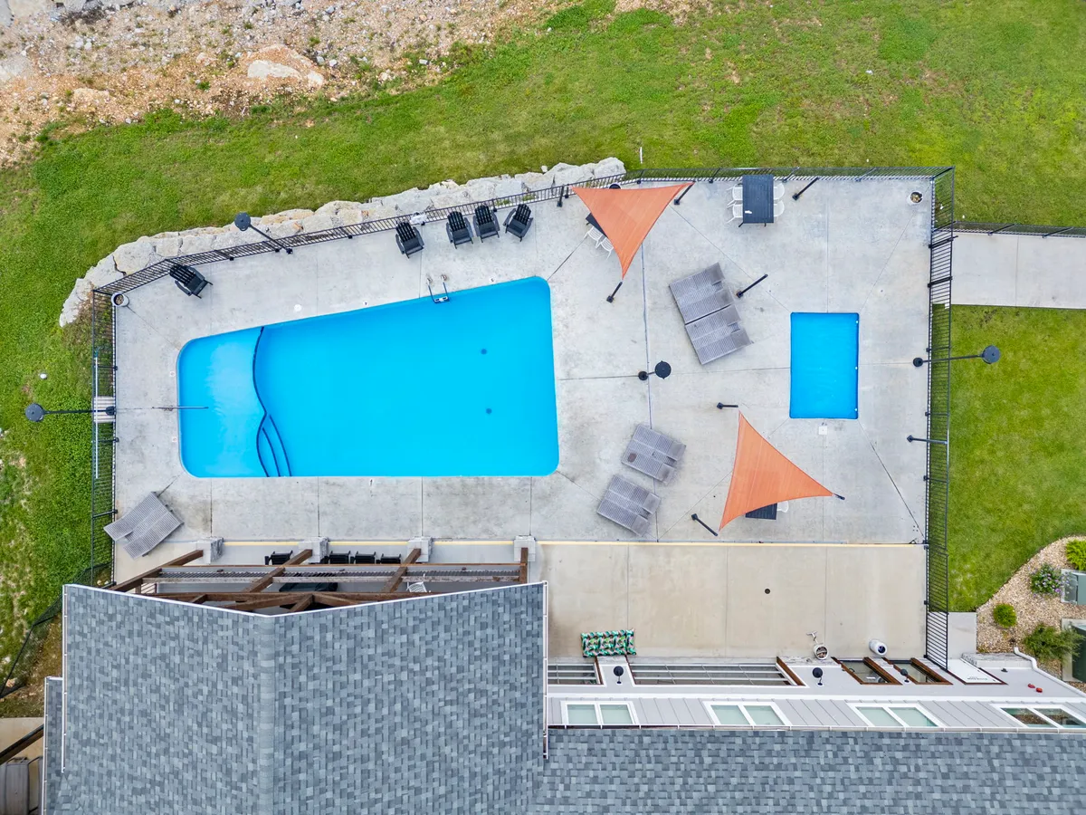 A vibrant exterior shot of a swimming pool with lounge chairs and shade sails, inviting guests to relax, swim, or socialize poolside. The pool area is surrounded by greenery and is ideal for families or groups seeking resort-style amenities.