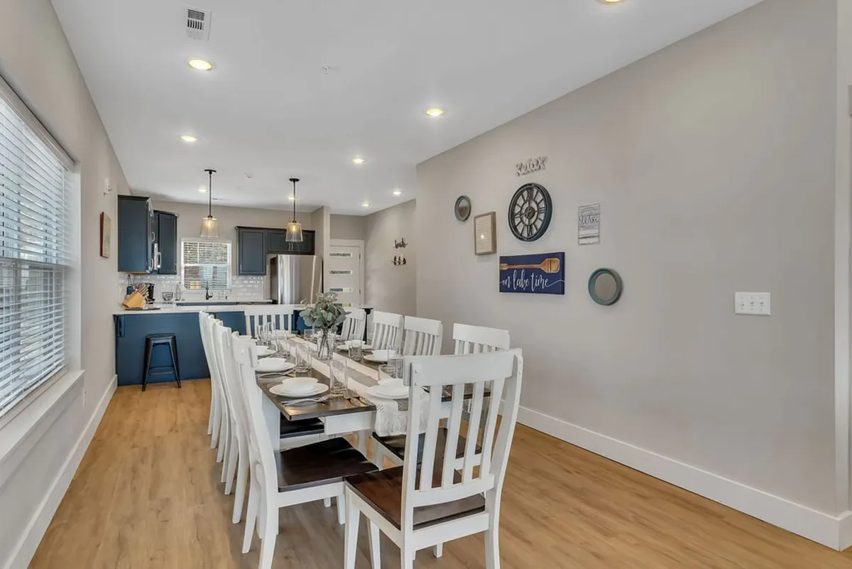 The image showcases a long dining table set in a space with blue kitchen cabinets and decorative wall art, ideal for hosting family gatherings, dinner parties, and holiday celebrations. The table invites a sense of togetherness, warmth, and shared meals.