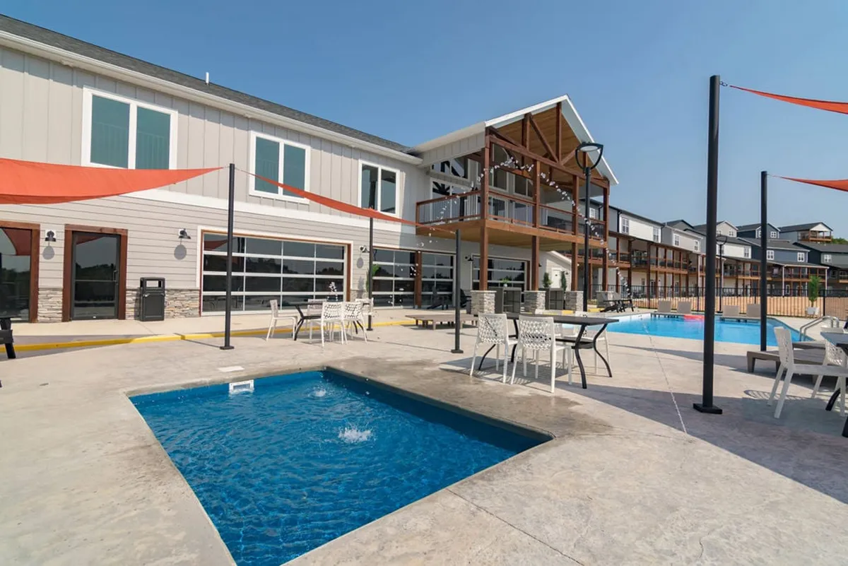 A cheerful exterior shot of the resort amenities, featuring the swimming pool, hot tub, and outdoor seating area. The scene includes people sunbathing and relaxing, with string lights creating an inviting environment for social gatherings and evening enjoyment.