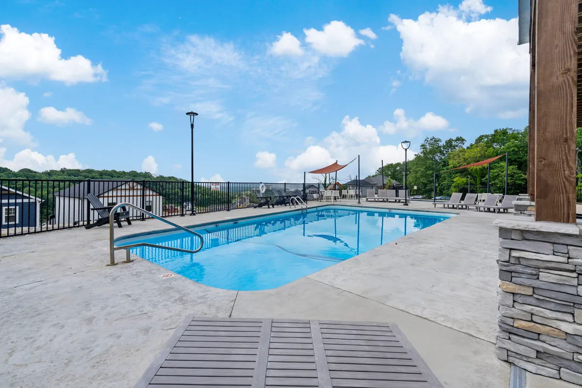 A sunlit outdoor swimming pool surrounded by lounge chairs, canopy shades, and lush greenery. The space is designed for socializing, sunbathing, or swimming, offering additional aquatic fun beyond the lake itself.