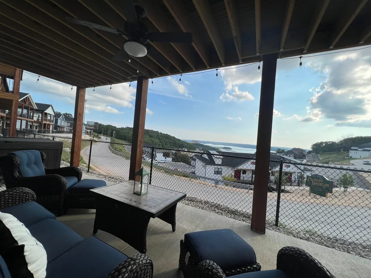 A tranquil outdoor seating area on the deck, complete with a coffee table, comfortable chairs, decorative lights, and scenic views of the hills and water. The space is set up for al fresco dining or lounging, perfect for both morning coffee and evening gatherings.