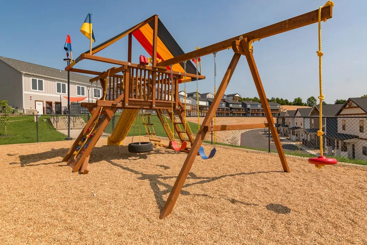 A vibrant children’s playground with colorful structures, swing sets, and flags, set in a safe outdoor area. Children are seen playing and families gather nearby, creating an atmosphere of fun and community.